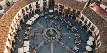 Vista aérea de una plaza española en festival, con patrones geométricos de adoquines y personas congregadas, celebrando la rica cultura y gastronomía tradicional.